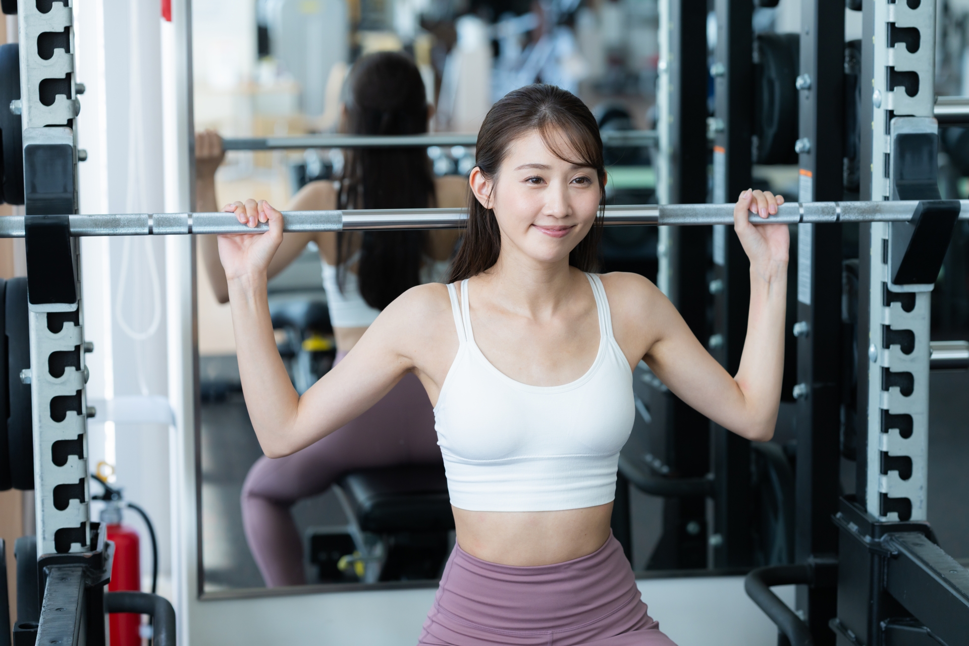 ジムでバーベルを担ぎ、笑顔でトレーニングする女性